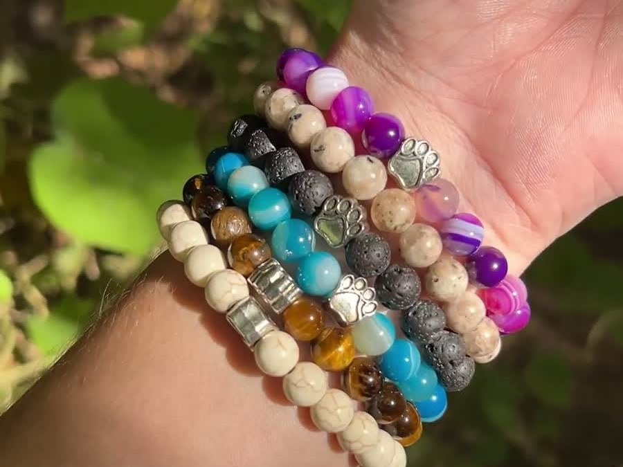 A wrist wearing five stacked Rescue Paws bracelets in different colors, in the sun