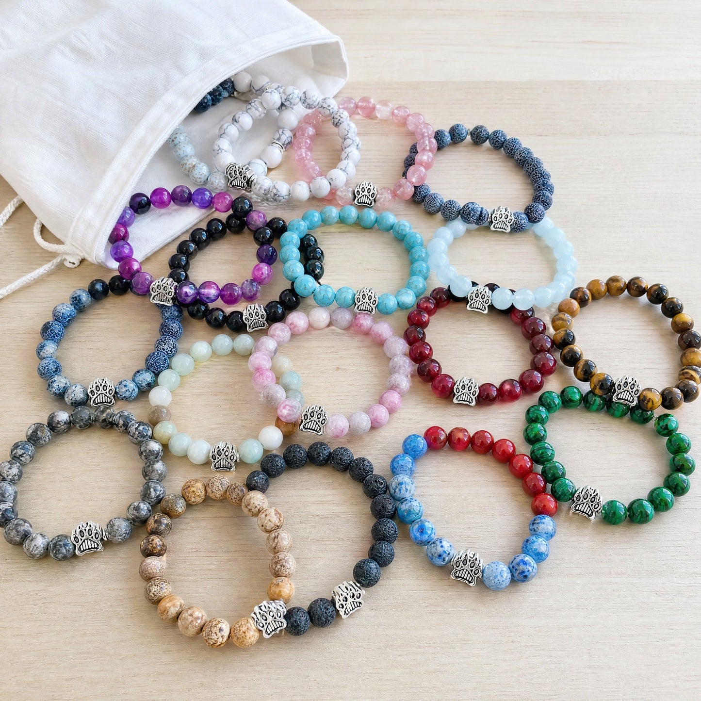 Twenty Rescue Paws beaded bracelets tipped out of a cotton pouch onto a wooden table