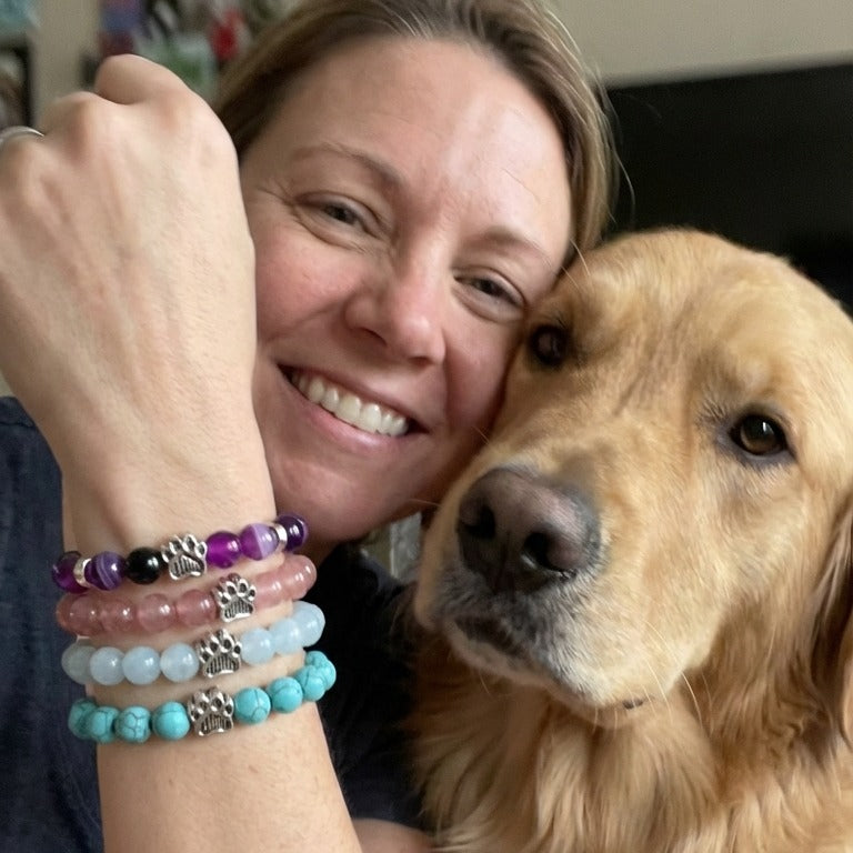 A smiling woman hugging her golden retriever, wearing Rescue Paws bracelets