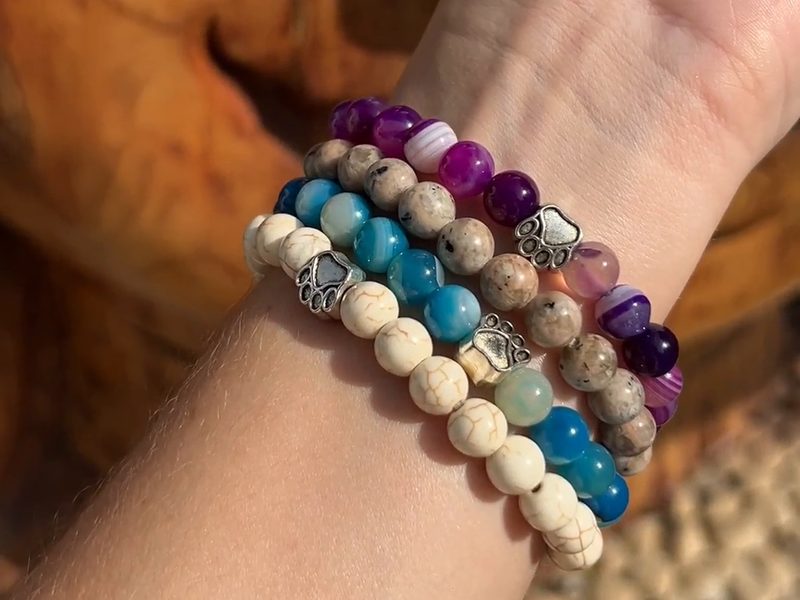 A wrist wearing a stack of Rescue Paws bead bracelets with paw charms